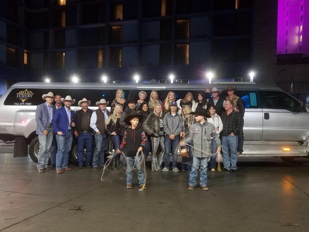 Large group of people in western attire outside large party bus at night Las Vegas event