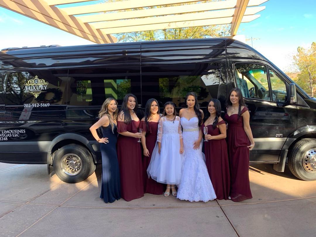 Bride in white gown and bridesmaids in burgundy dresses posing outside black Mercedes Sprinter Las Vegas wedding
