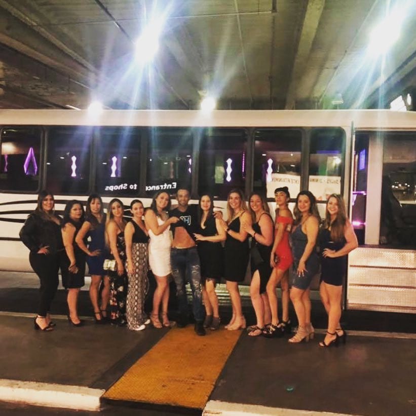Large bachelorette group posing outside white party bus Las Vegas at night