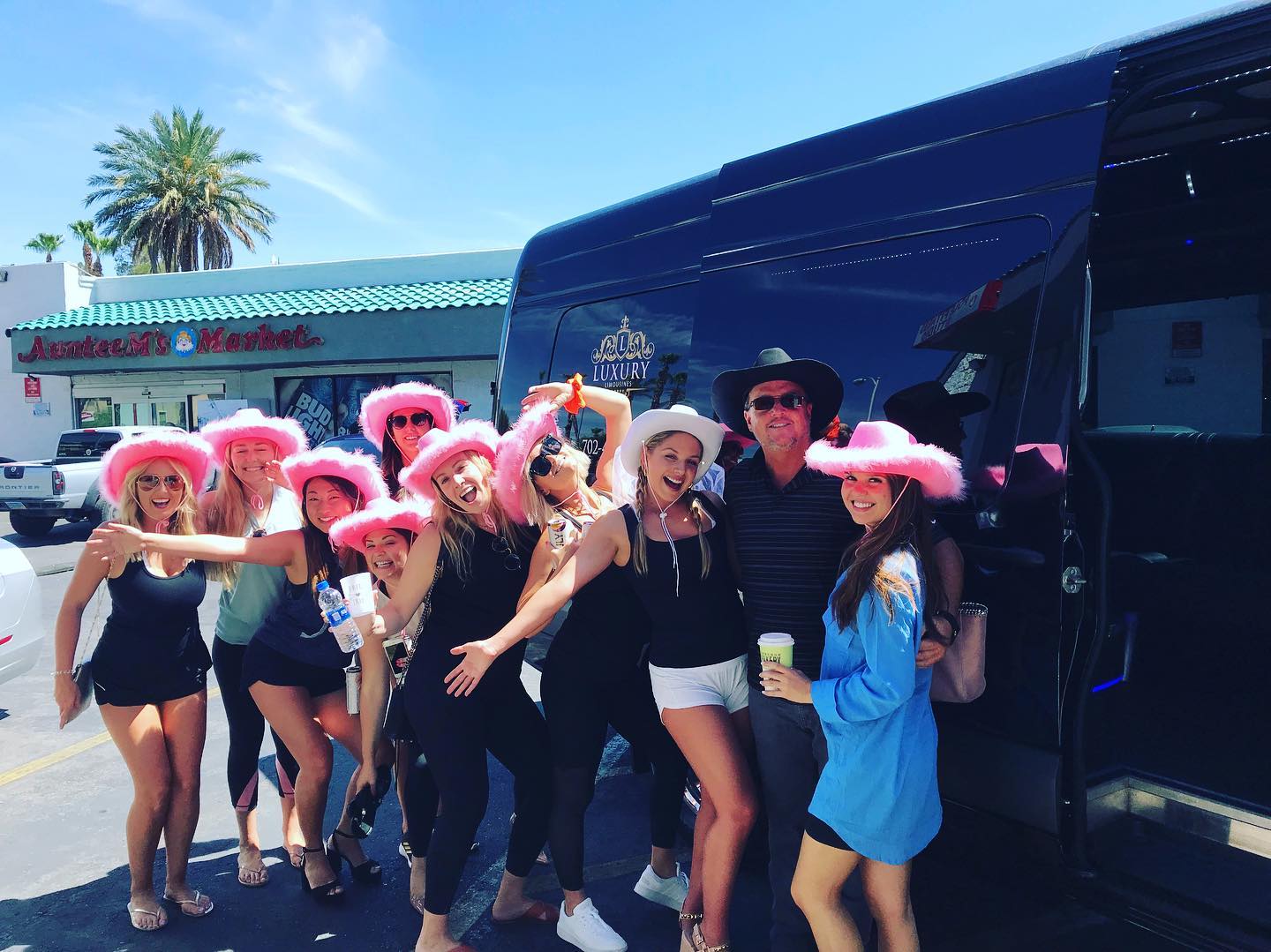 Bachelorette party group wearing pink cowboy hats outside black party bus Las Vegas daytime